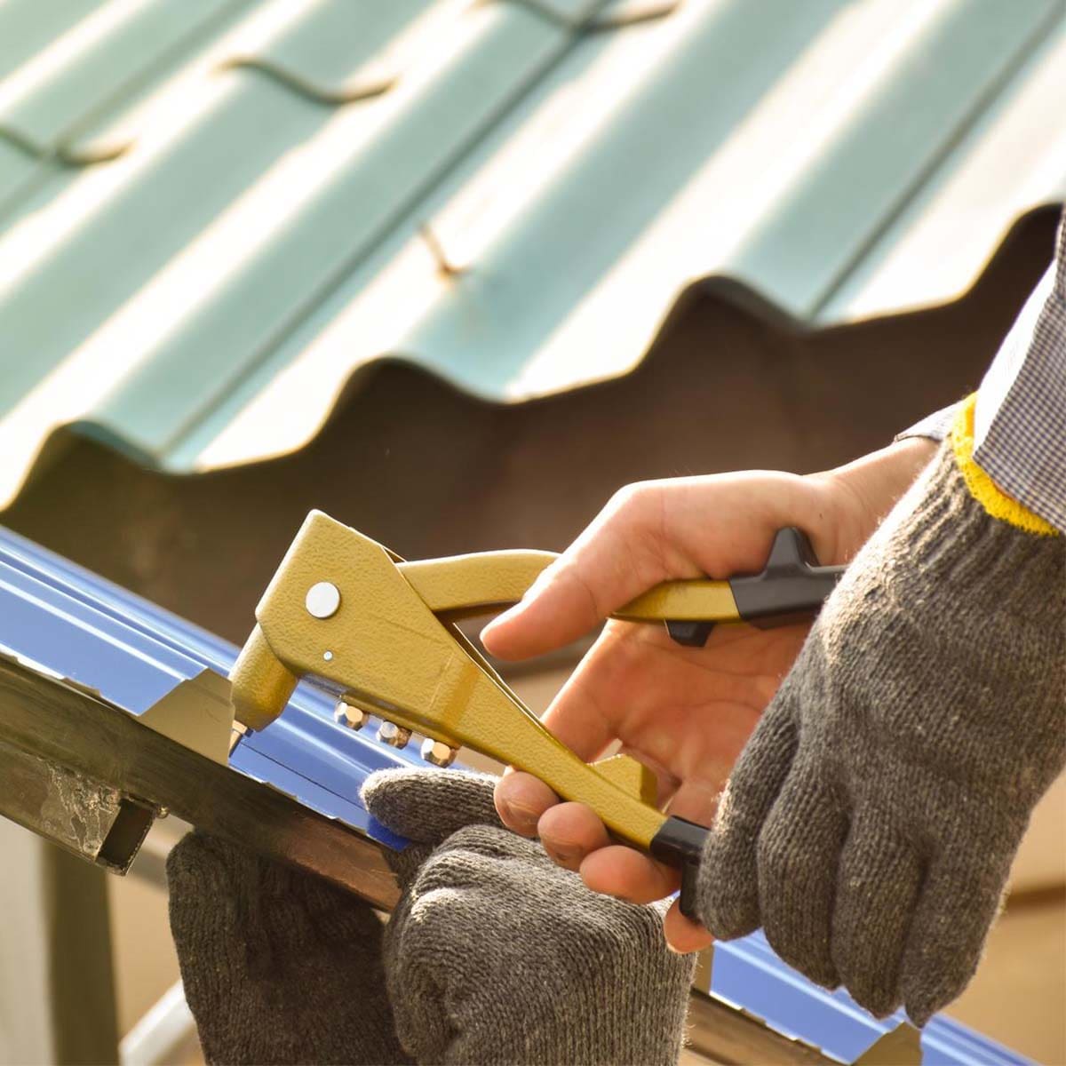 Roofer fixing a metal roof edge and gutter line with a hand tool